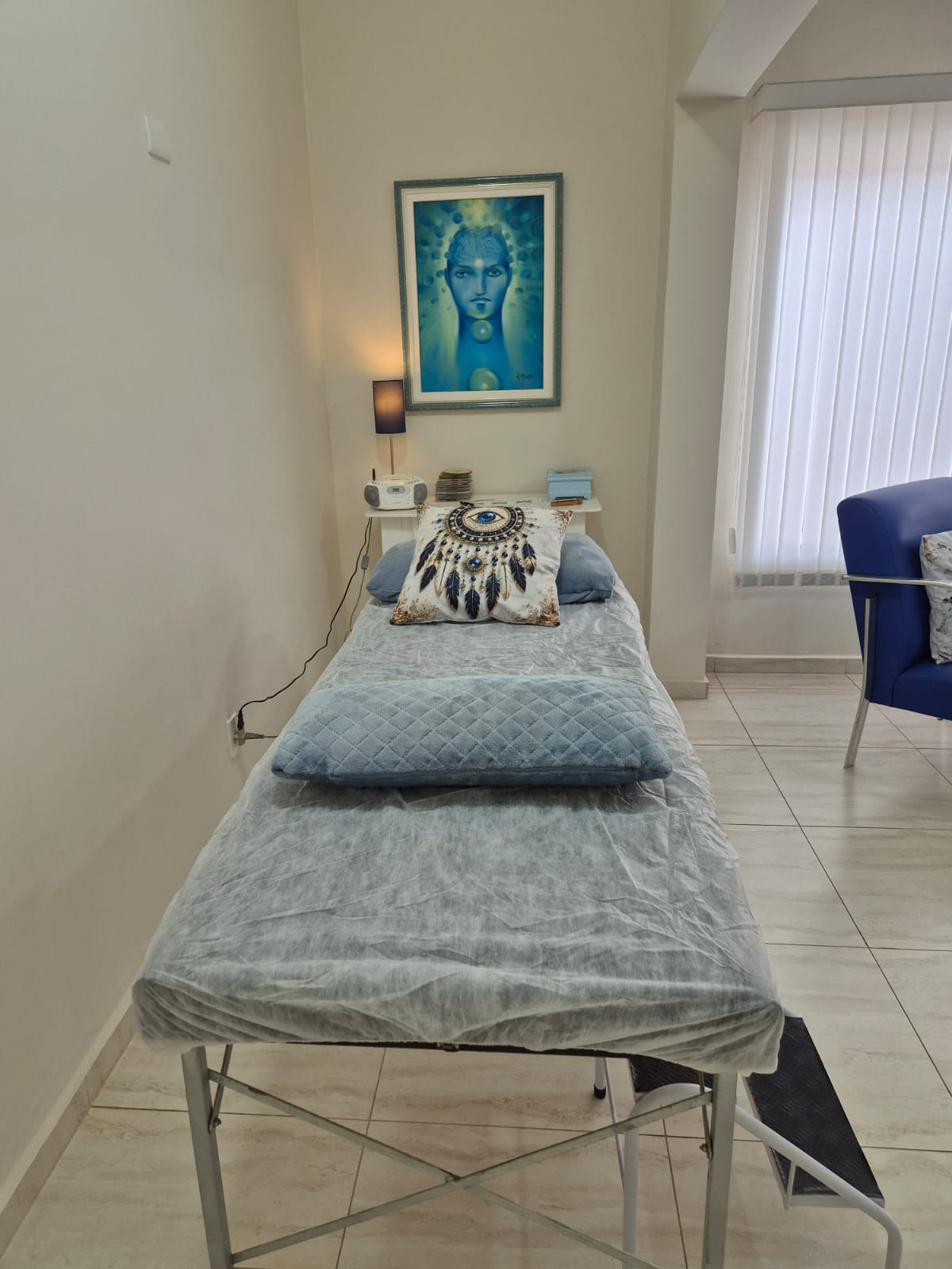 Espaço de relaxamento com maca, almofadas azuis, luminária e quadro em tons de azul